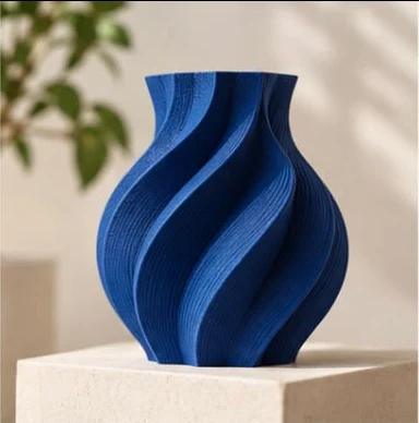 Vaso azul impresso em 3D, com curvas torcidas, sobre um pedestal de pedra